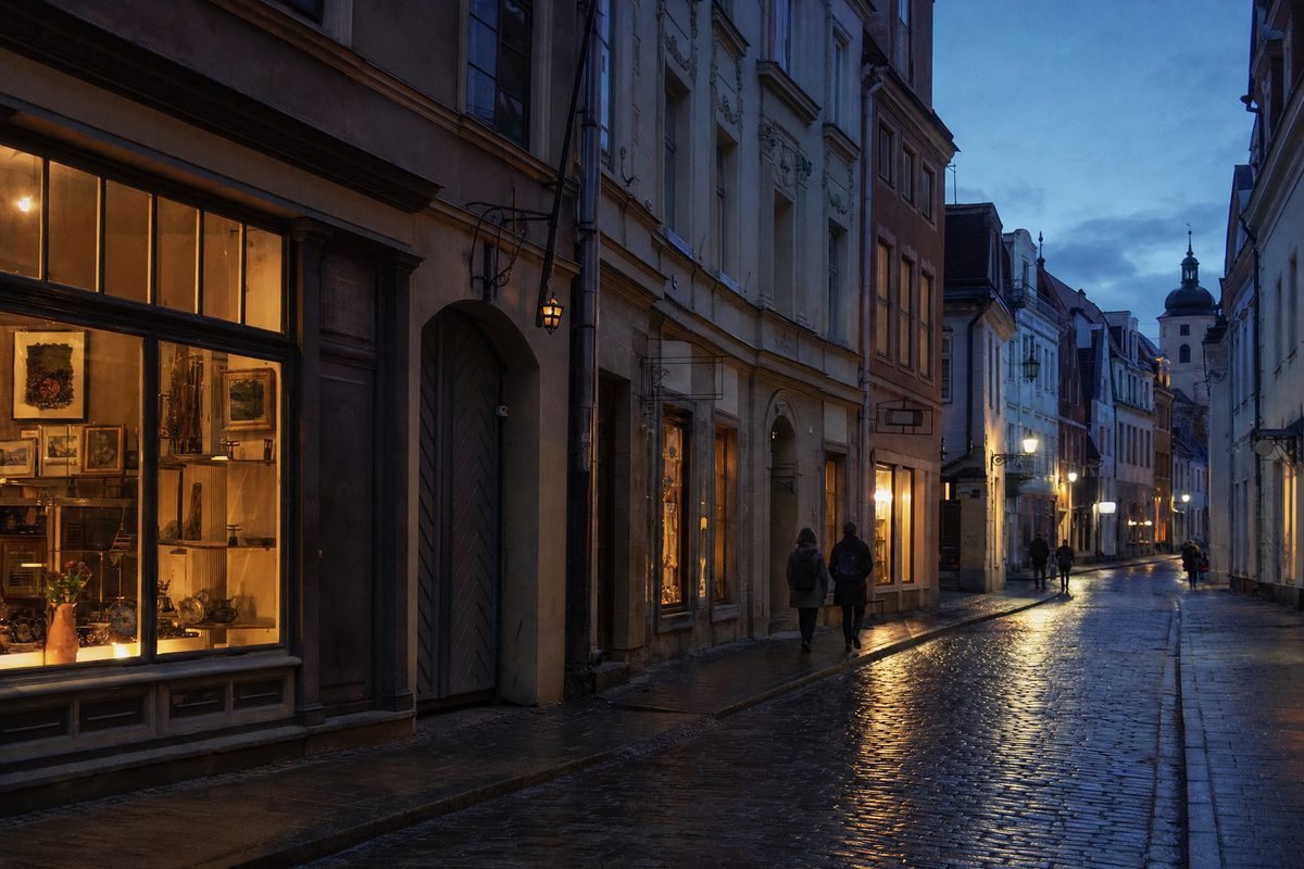 An old-town street at dusk with lit small shopfront windows