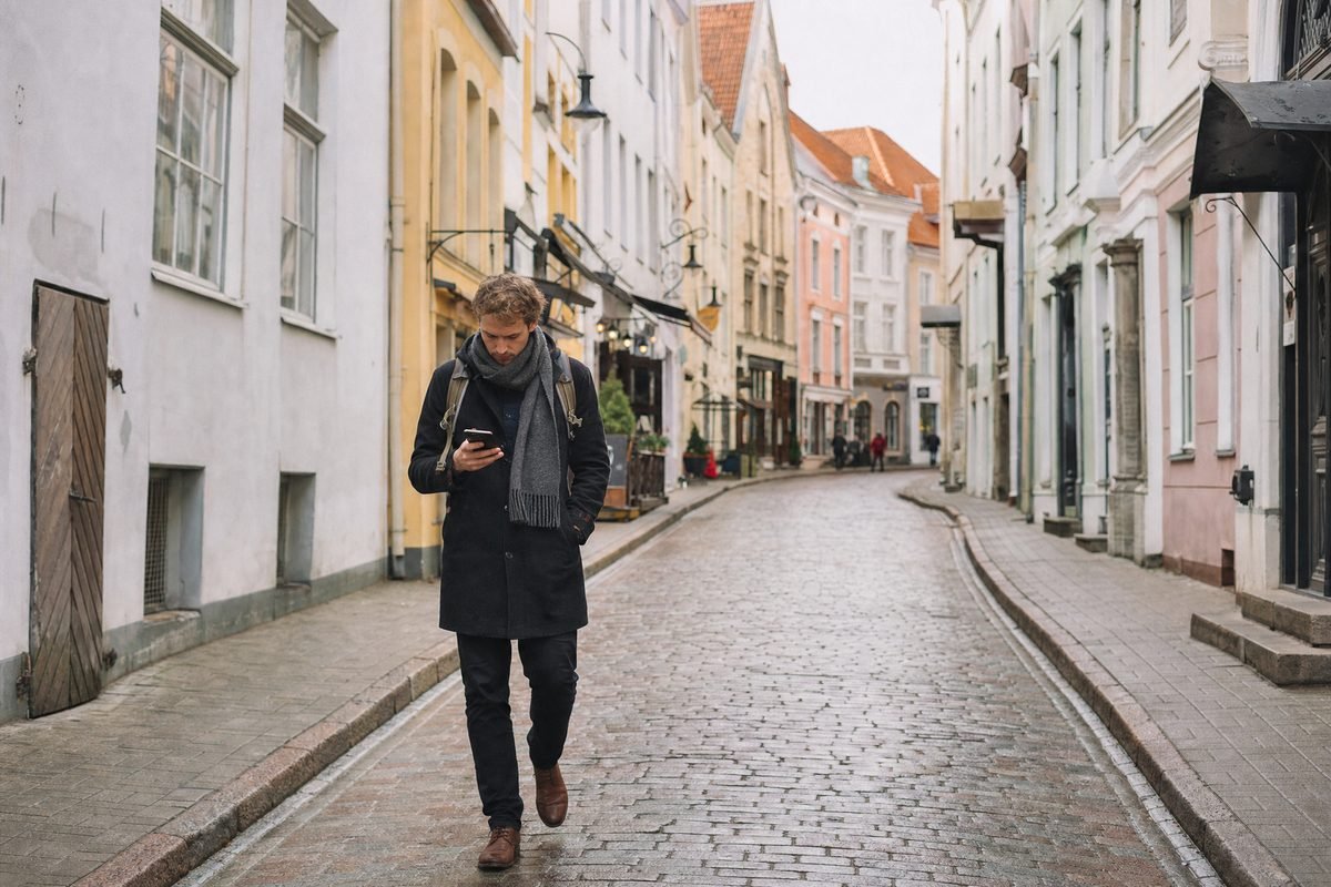 A person walking through an old-town street looking at a phone
