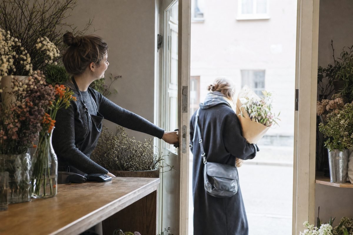 A flower shop owner holding the door for a departing customer